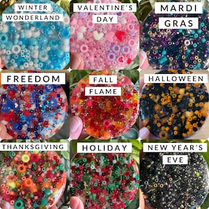 May include: Nine round resin coasters with different colored beads and glitter embedded in the resin. The coasters are labeled with the following holidays: Winter Wonderland, Valentine's Day, Mardi Gras, Freedom, Fall Flame, Halloween, Thanksgiving, Holiday, and New Year's Eve.