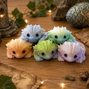 May include: A collection of five small, spiky, lizard-like figurines in pastel colors including light blue, peach, lime green, mint green, and lavender. Each figurine features a textured, bumpy surface, a rounded head, and two large black eyes.