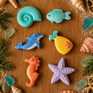May include: A collection of six colorful sea-themed decorative figures including a turquoise nautilus, a light blue fish, a blue dolphin, a yellow pineapple, an orange seahorse, and a purple starfish, arranged on a wooden surface with shells.