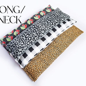 May include: Four long neck pillows stacked on top of each other. The pillows are made of fabric with different patterns: cherries, leopard print, black and white checkered, and leopard print. The pillows are on a white background.