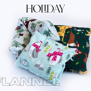 May include: Three flannel pillow covers with holiday-themed designs. The first pillow cover is green with a brown reindeer, a yellow tiger, and a white dog. The second pillow cover is blue with a white penguin and a pink scarf. The third pillow cover is white with green trees and red trucks. The text "HOLIDAY FLANNEL" is printed below the pillows.