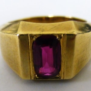 May include: A gold ring with a deep pink rectangular gemstone set in the center.