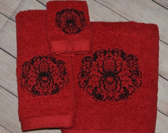 May include: Set of three red bath towels with black embroidered spider web designs. The towels are made of a soft, absorbent material.
