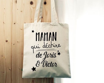 Op de afbeelding: Een witte canvas draagtas met zwarte tekst die "Maman qui déchire de Joris & Victor" luidt, met een ster aan weerszijden van de tekst.