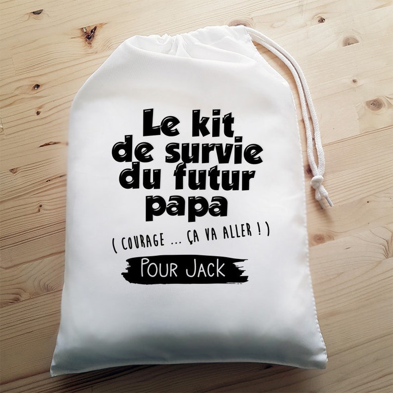 May include: White drawstring bag with black text that reads "Le kit de survie du futur papa (COURAGE... CA VA ALLER!)" and "POUR JACK".
