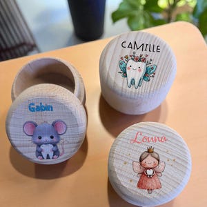 Könnte beinhalten: Zahnfee-Boxen aus Holz mit personalisierten Namen. Eine Box zeigt eine Maus, die einen Zahn hält, eine andere eine Zahnfee und die dritte einen Zahn mit Feenflügeln. Die Namen "Gabin", "Camille" und "Louna" sind auf den Boxen aufgedruckt.