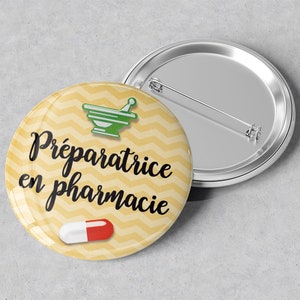 Puede incluir: Botón amarillo con un patrón de chevron y el texto "Préparatrice en pharmacie" en negro. También hay un mortero y un pilón verdes y una píldora roja y blanca en el botón.