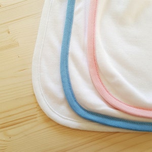 May include: Three white fabric bibs with different colored trim. The bibs have a blue, pink, and white trim.