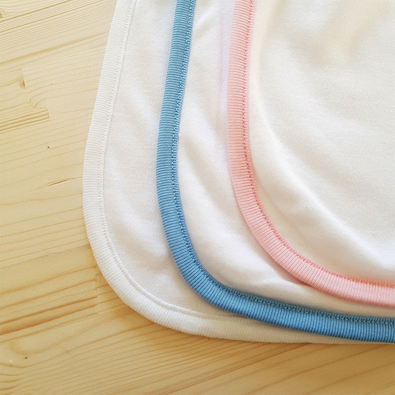 May include: Three white fabric bibs with different colored trim. The bibs have a blue, pink, and white trim.