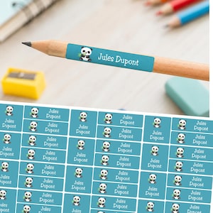 Puede incluir: Una hoja de etiquetas adhesivas rectangulares de color verde azulado con un panda de dibujos animados que sostiene un tallo de bambú verde y el texto blanco Jules Dupont. Una etiqueta está aplicada en un lápiz de madera con el nombre.