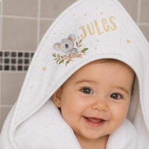 May include: White hooded baby towel with a koala bear illustration and the name "Jules" in gold lettering. The towel has a soft, plush texture and is decorated with small gold hearts.