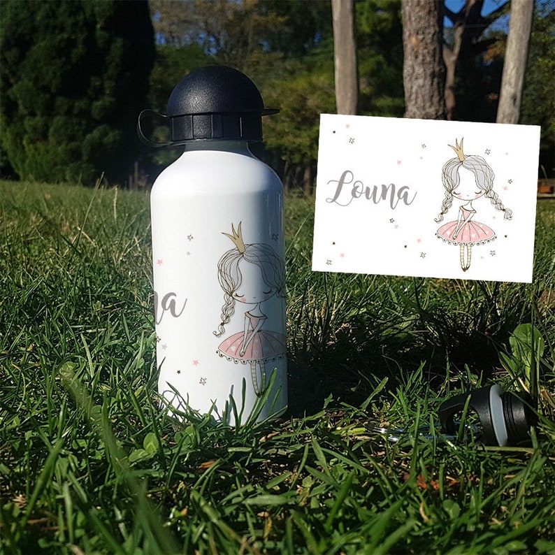 K&ouml;nnte beinhalten: Eine wei&szlig;e Wasserflasche mit einem rosa-wei&szlig;en Prinzessinnen-Design und dem Namen Louna. Die Flasche hat einen schwarzen Deckel und einen schwarzen Trageriemen.