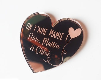 May include: A rose gold heart-shaped acrylic plaque with the text "On t'aime Mamie!" and the names "Nino, Mattia & Chloe" engraved on it. A small pink heart balloon is also engraved on the plaque.