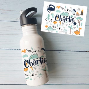 Könnte beinhalten: Weiße Trinkflasche mit schwarzem Deckel und Strohhalm, verziert mit einem Dinosaurier-Thema. Die Flasche trägt den Namen "Charlie" in einer verspielten Schriftart, zusammen mit verschiedenen Dinosaurier-Illustrationen in Blau-, Orange- und Grüntönen.