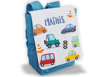 May include: A blue and white backpack with a personalized name "MATHIS" and a colorful car design. The backpack has a mesh pocket on the side and a zippered pocket on the front.