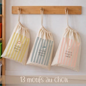 Pode incluir: Três sacos de cordão em tom creme com riscas verticais em amarelo, azul-acinzentado e rosa. Cada saco apresenta uma pequena ilustração de animal e texto em francês: Les p'tites affaires de Leon, Les p'tites affaires de Marius e le sac de change de Juliette.