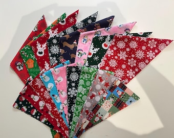 May include: A collection of triangular fabric bandanas featuring various Christmas-themed prints including snowmen, reindeer, snowflakes, Santa Claus, and gingerbread houses in vibrant colours like red, green, blue, pink, and black.