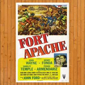 May include: A vintage movie poster for the film "Fort Apache" starring John Wayne, Henry Fonda, Shirley Temple, and Pedro Armendariz. The poster features a scene of a battle between soldiers and Native Americans, with a red and white title card.