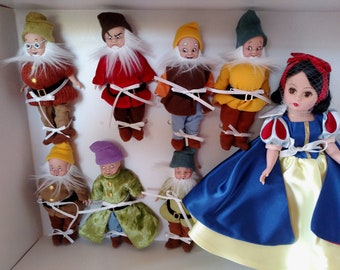May include: A collection of vintage Snow White and the Seven Dwarfs dolls. The dwarfs are dressed in colorful outfits with white beards and hats. Snow White is in a blue and yellow dress with a red bow.