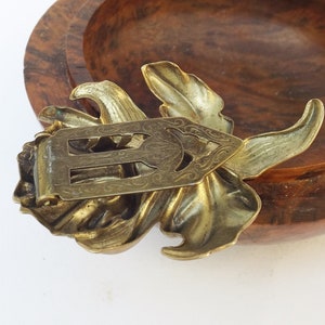 May include: A gold-toned metal flower brooch with an intricate design. The brooch has a floral shape with a detailed center and a clasp on the back.
