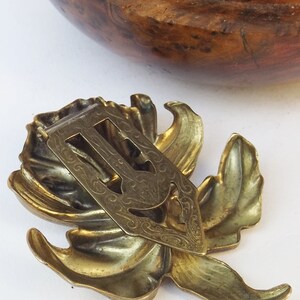 May include: A gold-toned metal hair clip in the shape of a stylized flower with intricate details. The clip has a decorative back with a floral design.