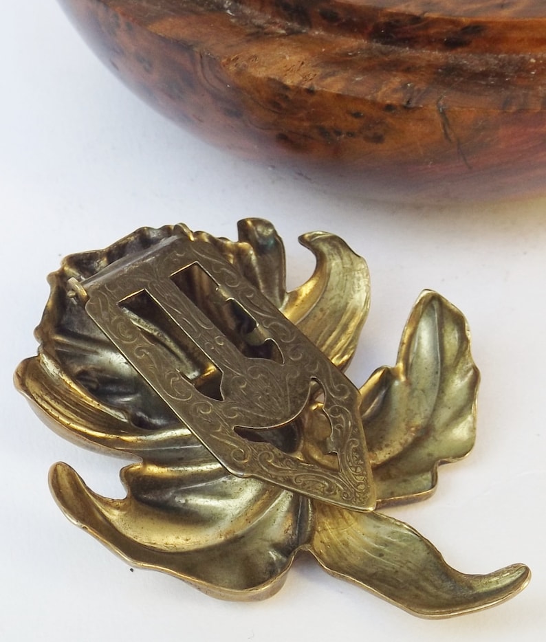 May include: A gold-toned metal hair clip in the shape of a stylized flower with intricate details. The clip has a decorative back with a floral design.
