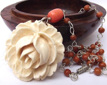 May include: A carved ivory rose pendant on a brown wooden bead and silver chain necklace with a coral bead accent.