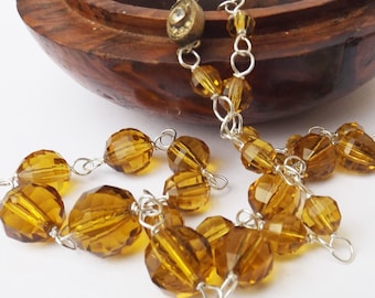 May include: A gold-toned chain necklace with amber-colored glass beads. The necklace is displayed in a wooden box.