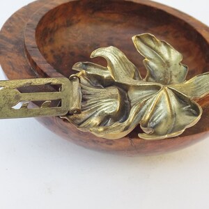 May include: A gold-toned metal brooch with a leaf design. The brooch has a decorative clasp.