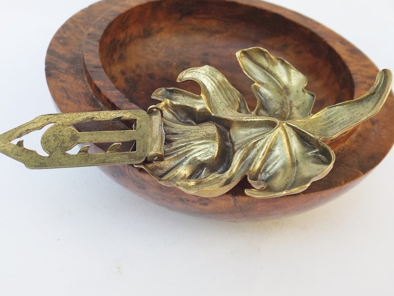 May include: A gold-toned metal brooch with a leaf design. The brooch has a decorative clasp.