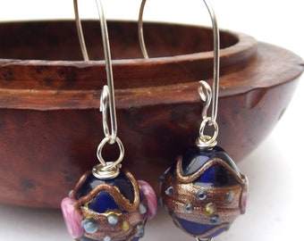 May include: A pair of silver dangle earrings with blue and gold glass beads. The beads have a textured surface and are decorated with pink, gold, and blue accents.