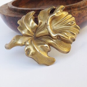 May include: A gold-toned metal brooch in the shape of a stylized flower with a large, open bloom and leaves.
