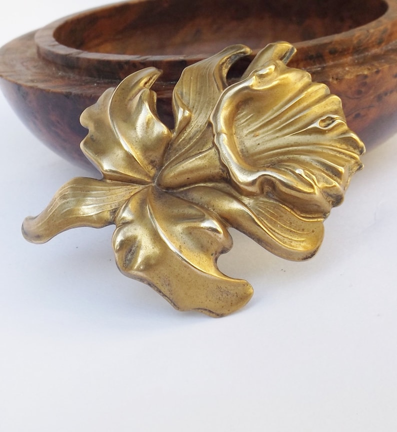 May include: A gold-toned metal brooch in the shape of a stylized flower with a large, open bloom and leaves.