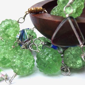 May include: A green glass necklace with a triangular clear glass pendant and silver chain. The necklace features multiple green glass beads with a textured surface.