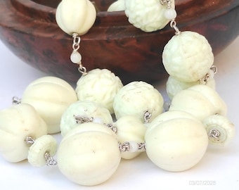 May include: A necklace featuring pale off-white, spherical beads with carved floral and ribbed textures. The beads are connected by thin silver-toned metal links and small, round, translucent white spacer beads, creating a layered, textured appearance.