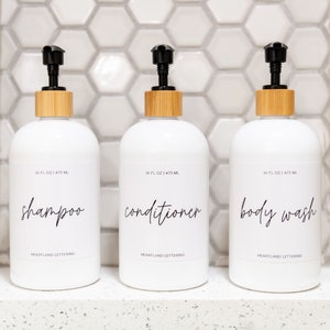 Set of 3 reusable plastic bottles to declutter and organize your shower! 16. oz. white plastic bottle set includes shampoo, conditioner and body wash in a modern script style. Part of the Classic Series by Heartland Lettering.