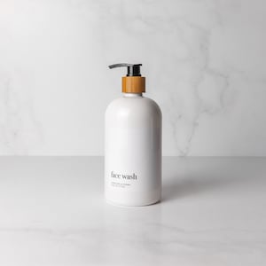 Minimalist style refillable white plastic shampoo bottle with black bamboo pump on an organized decluttered marble bathroom counter. Holds 16 fluid ounces/500 milliliters and comes in a set of 4 with shampoo, conditioner, and face wash.
