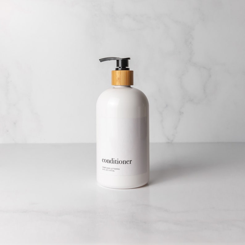 Minimalist style refillable white plastic conditioner bottle with black bamboo pump on an organized decluttered marble bathroom counter. Holds 16 fluid ounces/500 milliliters and comes in a set of 4 with shampoo, body wash and face wash.