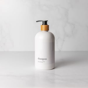 Minimalist style refillable white plastic shampoo bottle with black bamboo pump on an organized decluttered marble bathroom counter. Holds 16 fluid ounces/500 milliliters and comes in a set of 4 with conditioner, body wash and face wash.
