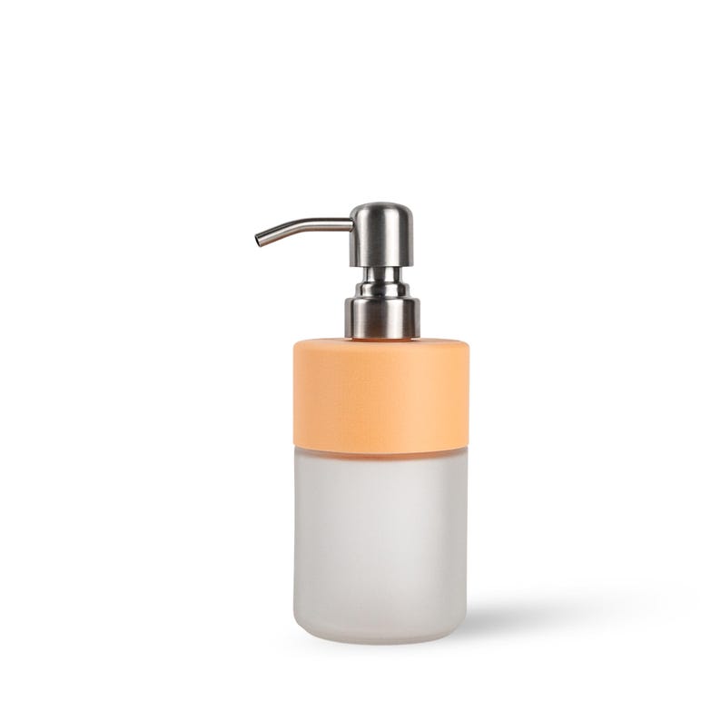 Op de afbeelding: Een moderne zeepdispenser met een basis van matglas en een perzikkleurige bovenkant. De dispenser heeft een zilveren pomp en tuit. Het ontwerp is minimalistisch en geschikt voor een badkamer of keuken.