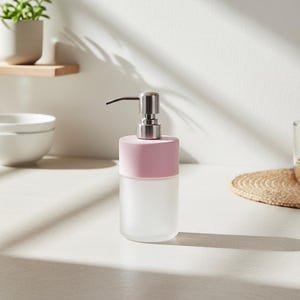 Op de afbeelding: Een zeepdispenser van matglas met een roze bovenkant en een zilveren pomp. De dispenser is cilindrisch en staat op een wit oppervlak. Het ontwerp is minimalistisch en modern, geschikt voor een badkamer of keuken.