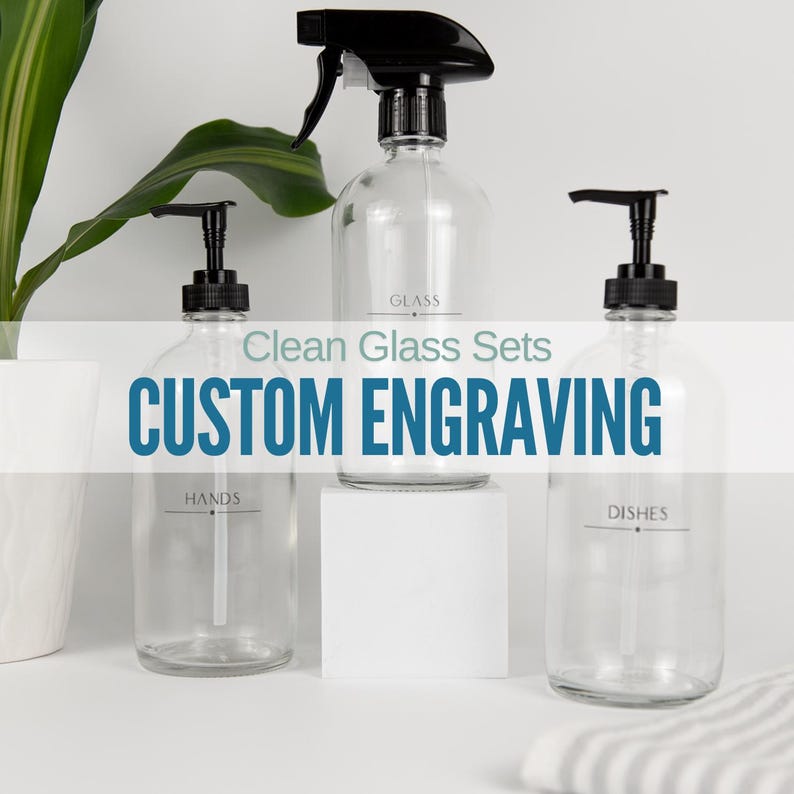 May include: Three clear glass bottles with black pump tops and labels. The labels read "GLASS", "HANDS", and "DISHES". The bottles are on a white surface with the text "Clean Glass Sets CUSTOM ENGRAVING" in blue.