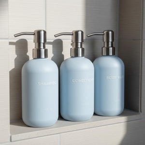 May include: Three light blue, refillable bathroom bottles with silver pump dispensers. The bottles are labeled "SHAMPOO", "CONDITIONER", and "BODY WASH". Each bottle holds 8 fl oz.