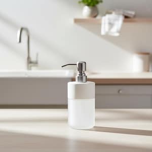 Op de afbeelding: Een witte en matglazen zeepdispenser met een zilveren pomp. De dispenser heeft een cilindrische vorm met een wit bovenstuk. Het ontwerp is minimalistisch en modern, geschikt voor een keuken of badkamer.