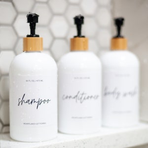 Set of 3 reusable plastic bottles to declutter and organize your shower! 16. oz. white plastic bottle set includes shampoo, conditioner and body wash in a modern script style. Part of the Classic Series by Heartland Lettering.