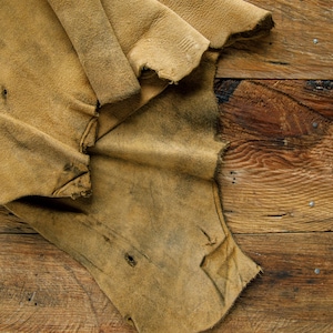 Puede incluir: Un trozo de cuero marr&oacute;n con un aspecto desgastado y envejecido. El cuero est&aacute; doblado y tiene una textura rugosa. Est&aacute; sobre una superficie de madera.