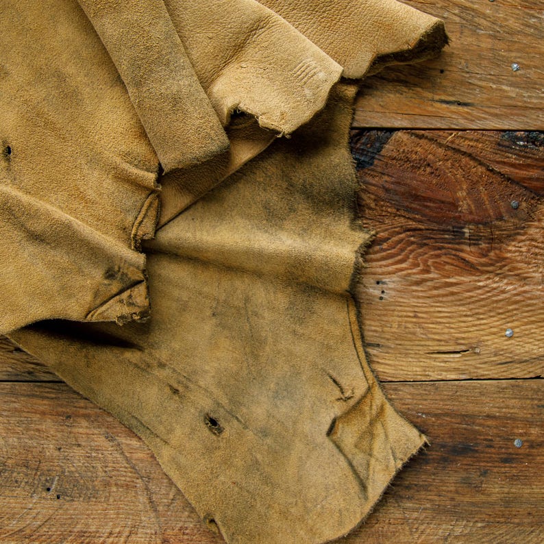 Puede incluir: Un trozo de cuero marr&oacute;n con un aspecto desgastado y envejecido. El cuero est&aacute; doblado y tiene una textura rugosa. Est&aacute; sobre una superficie de madera.