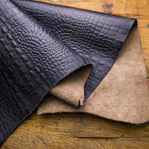 May include: Two pieces of leather, one black and one brown, with a crocodile-embossed pattern. The black leather is folded over the brown leather.