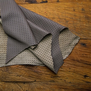 Puede incluir: Un trozo de tela de cuero perforada gris y beige doblado sobre una superficie de madera.
