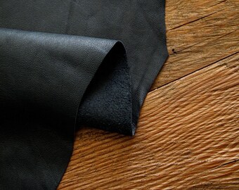 May include: A piece of black leather folded over on a wooden surface. The leather has a smooth, textured surface.